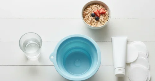 A flat lay of at-home remedies for hemorrhoid relief, including a sitz bath, soothing cream, and high-fiber food, arranged on a clean white table.
